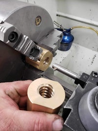 a person is holding a brass nut on a lathe